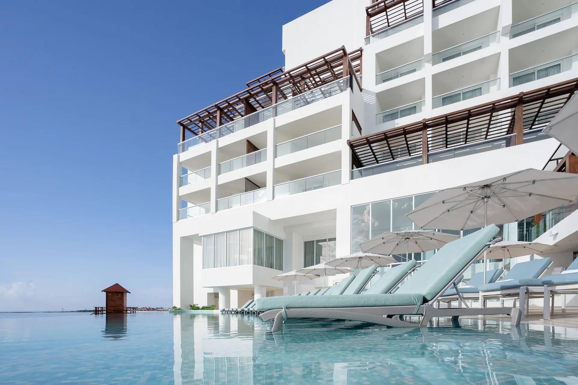 Poolside loungers sit in shallow water beside the white resort building at Sun Palace Cancun.