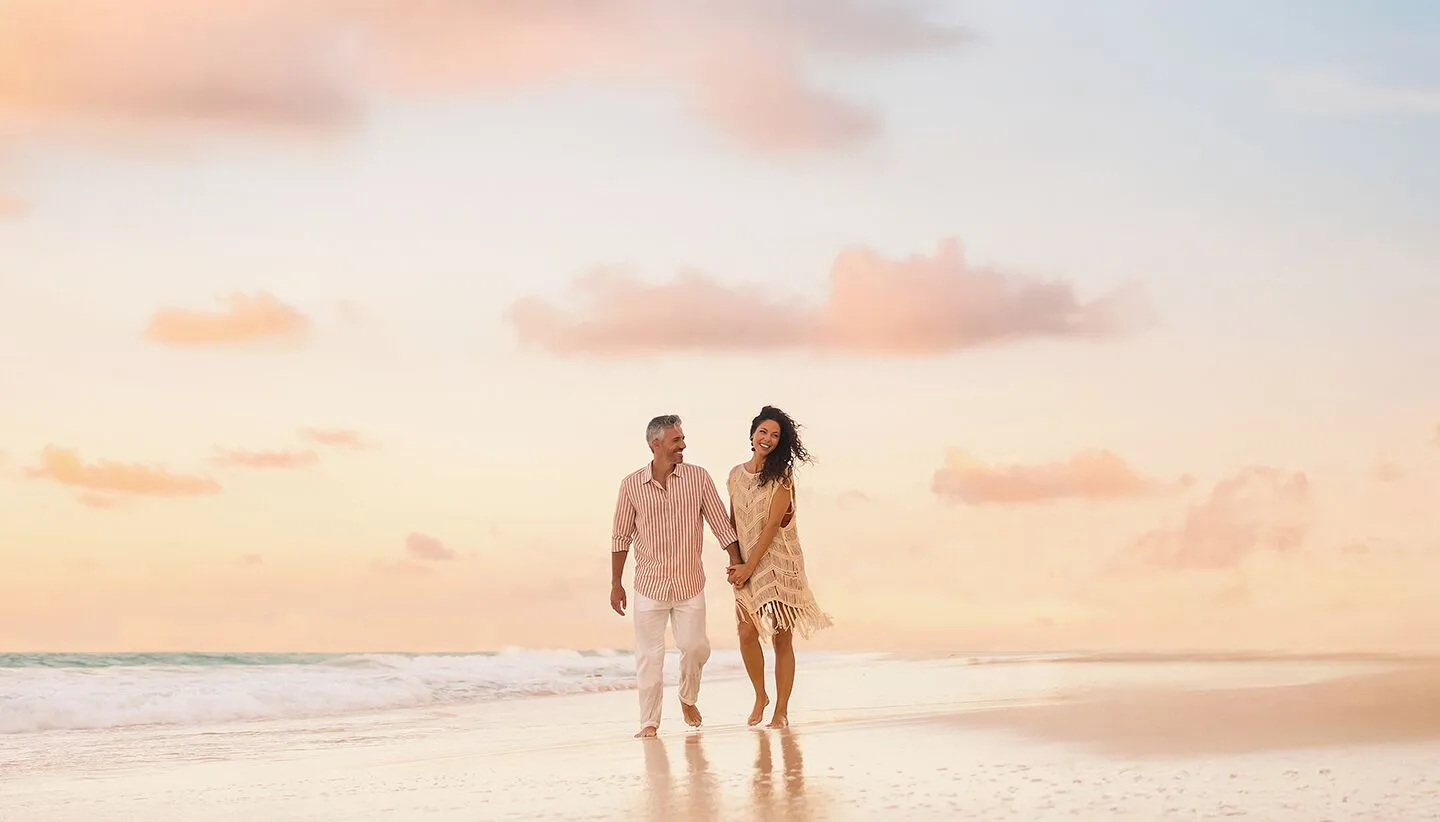 A couple walks hand in hand along the beach at sunset at Sun Palace Cancun.