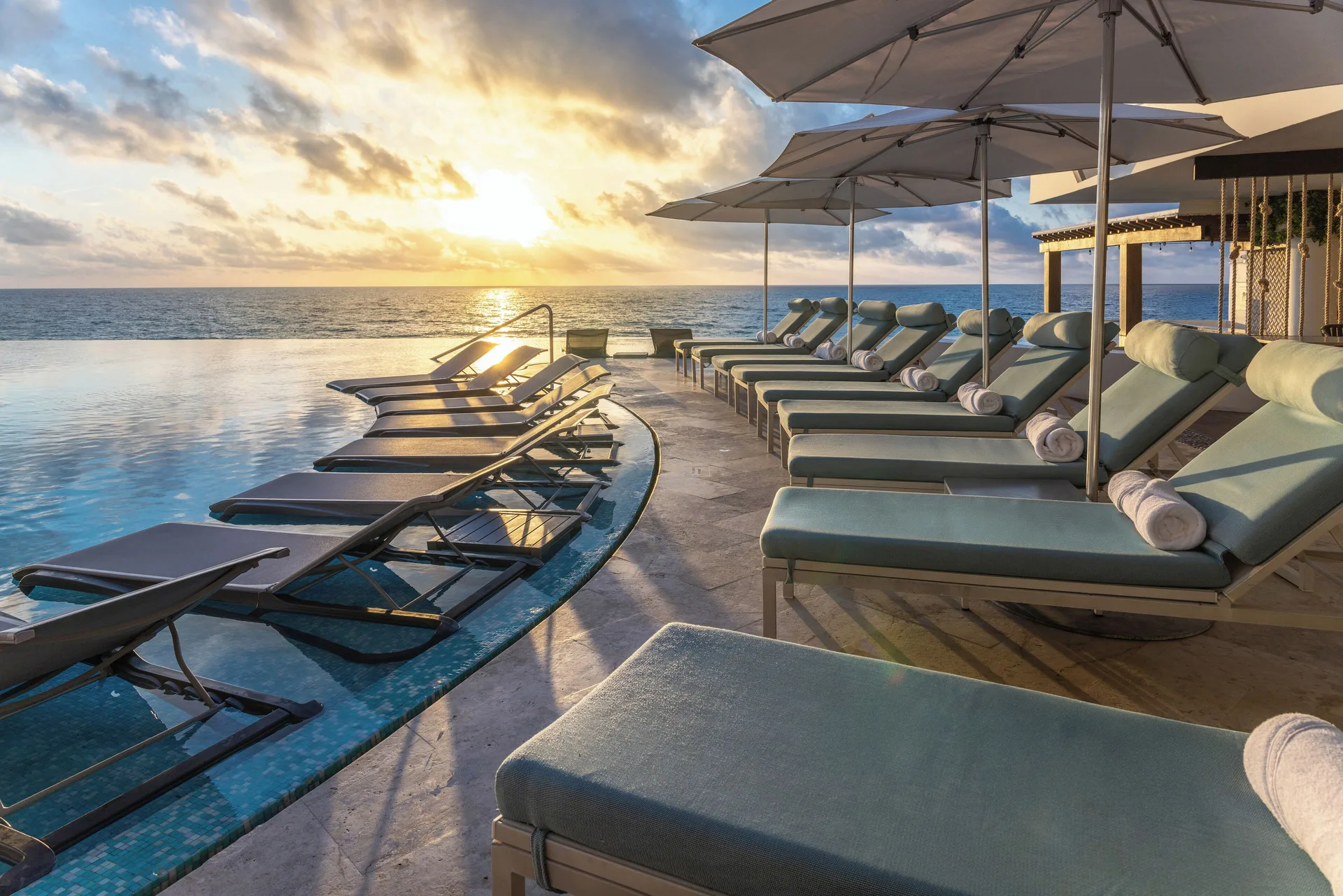 Poolside loungers with umbrellas face the ocean at sunset at Sun Palace Cancun.