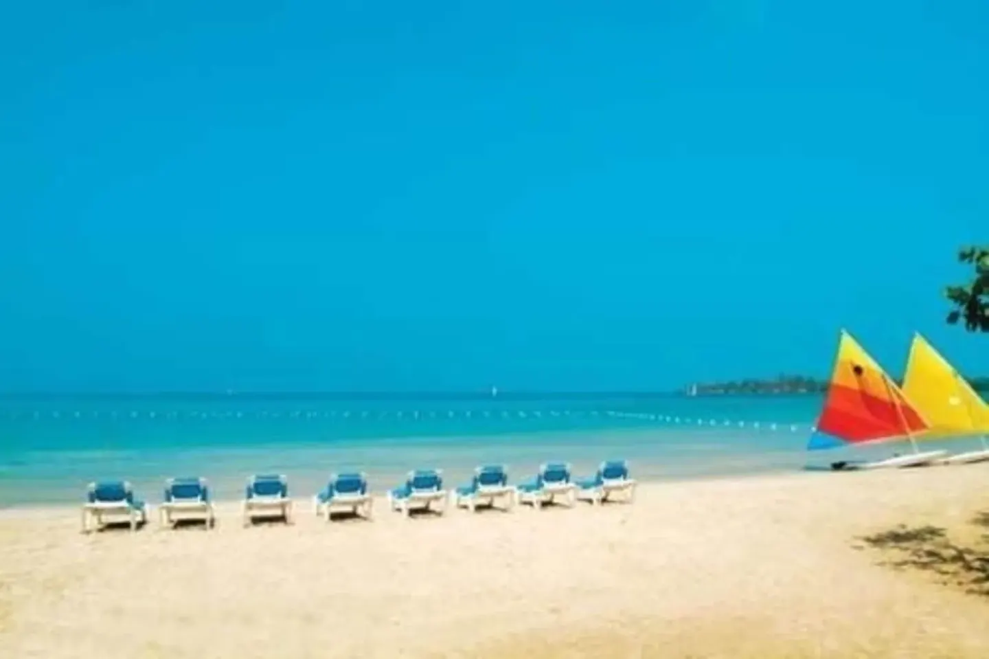 Blue lounge chairs and colorful sailboats line the beach at Sunset at the Palms Resort.