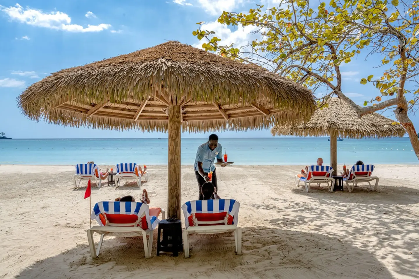 Thatched beach umbrellas shade lounge chairs and guests at Sunset at the Palms Resort.