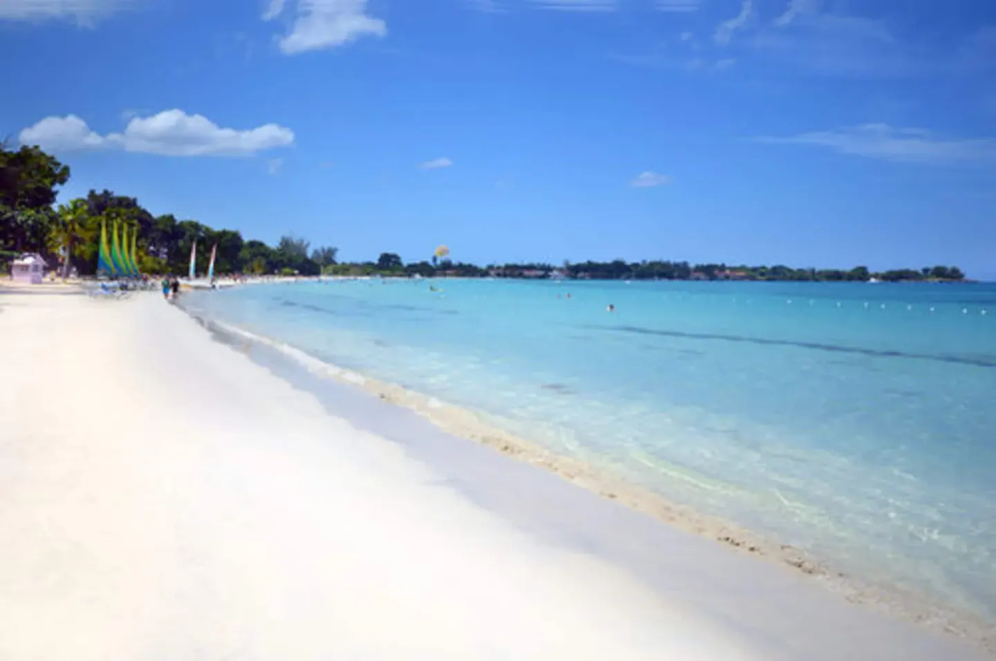 A wide sandy beach curves beside clear blue water at Sunset at the Palms Resort.