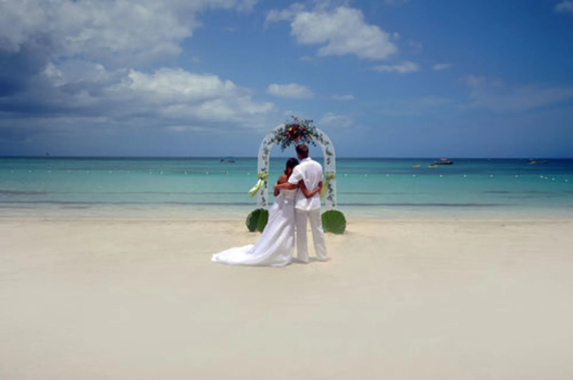 Bride and groom facing a beach wedding arch at Sunset at the Palms Resort.