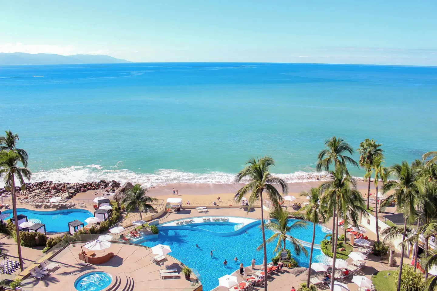 Beachfront pools, palms, and ocean at Sunset Plaza Beach Resort & Spa Pto Vallarta.