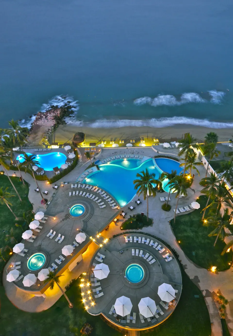 Evening aerial view of lit pools and beach at Sunset Plaza Beach Resort & Spa Pto Vallarta.