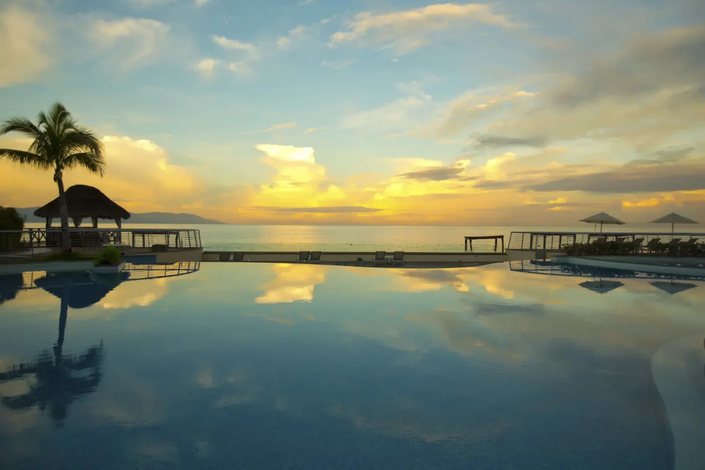 Infinity pool reflecting sunset over the ocean at Sunset Plaza Beach Resort & Spa Pto Vallarta.