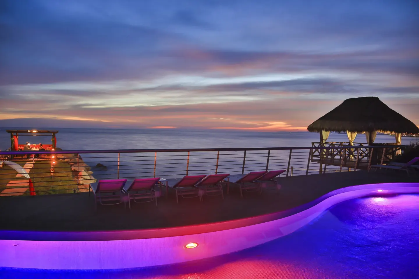 Pool deck glowing at dusk by the ocean at Sunset Plaza Beach Resort & Spa Pto Vallarta.
