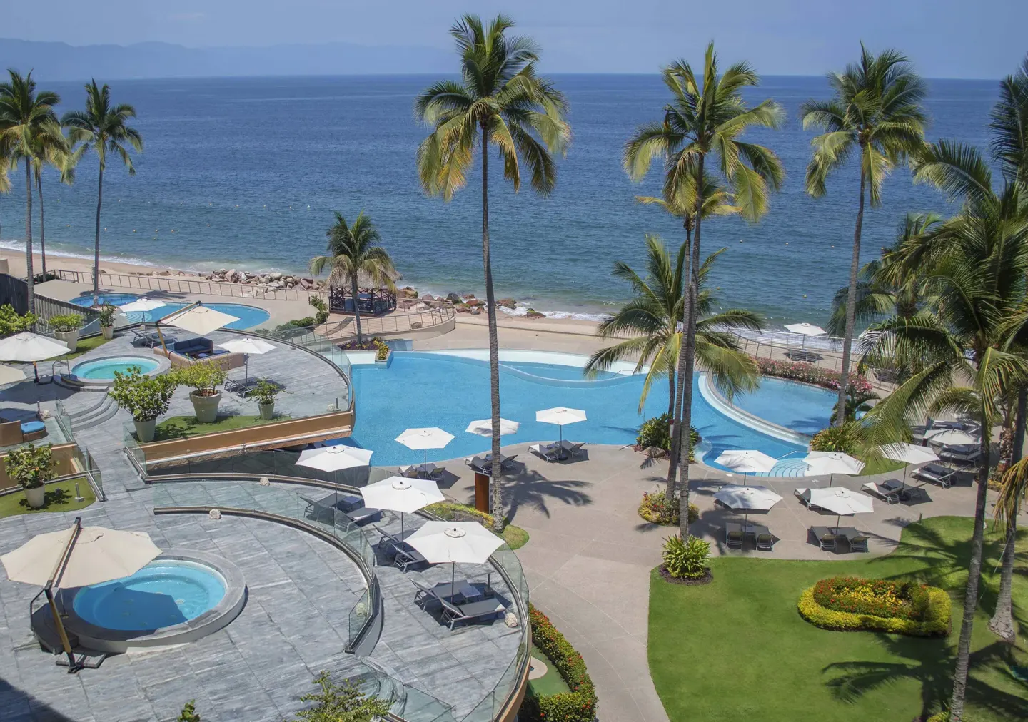 Oceanfront pools, loungers, umbrellas, and palms at Sunset Plaza Beach Resort & Spa Pto Vallarta.