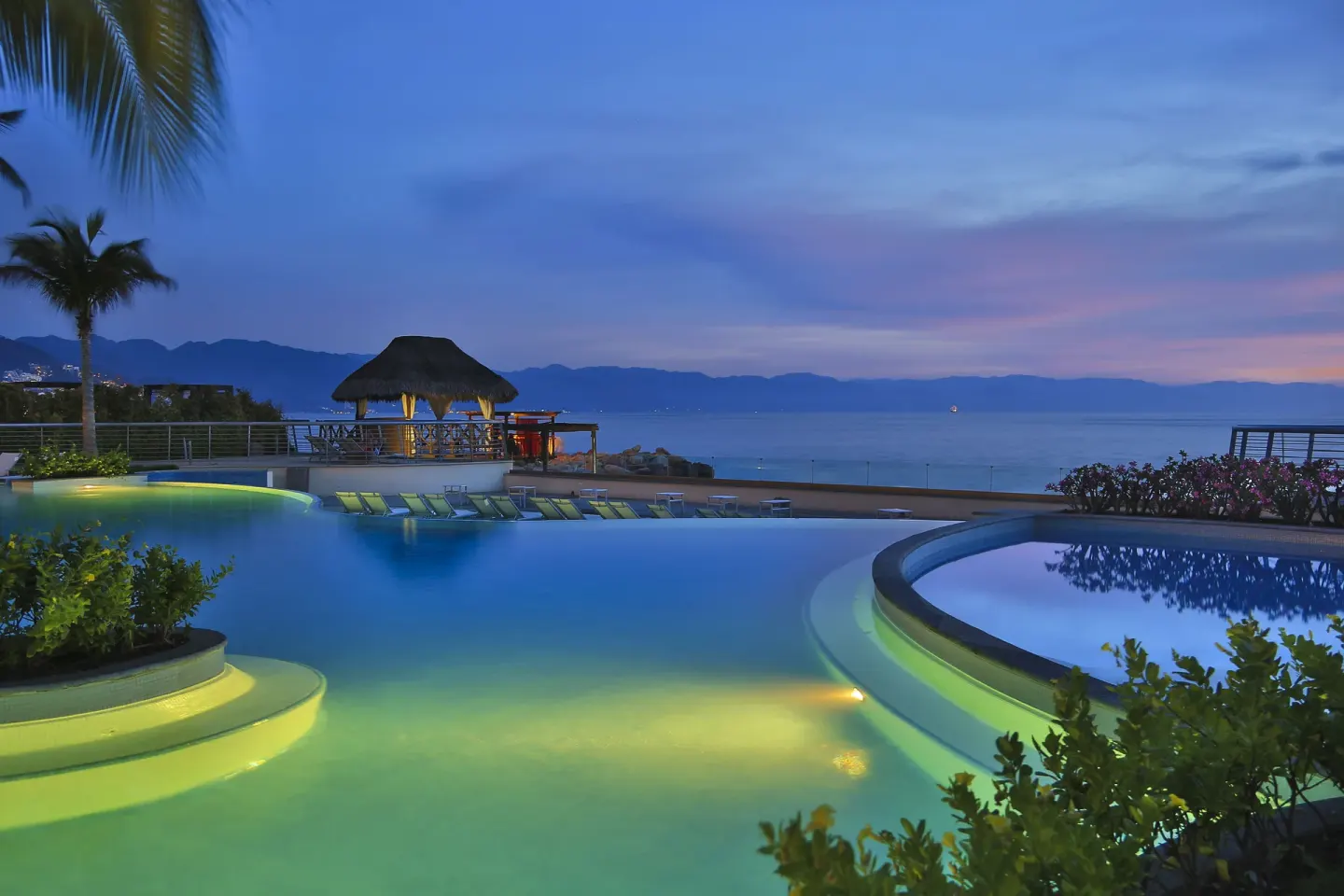 Illuminated pool and ocean at dusk at Sunset Plaza Beach Resort & Spa Pto Vallarta.