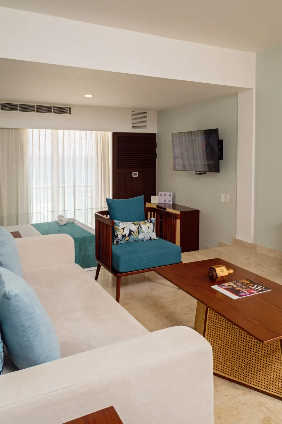 Guest suite seating area with sofa, bed edge, TV, and balcony curtains at Sunset Royal Beach Resort.