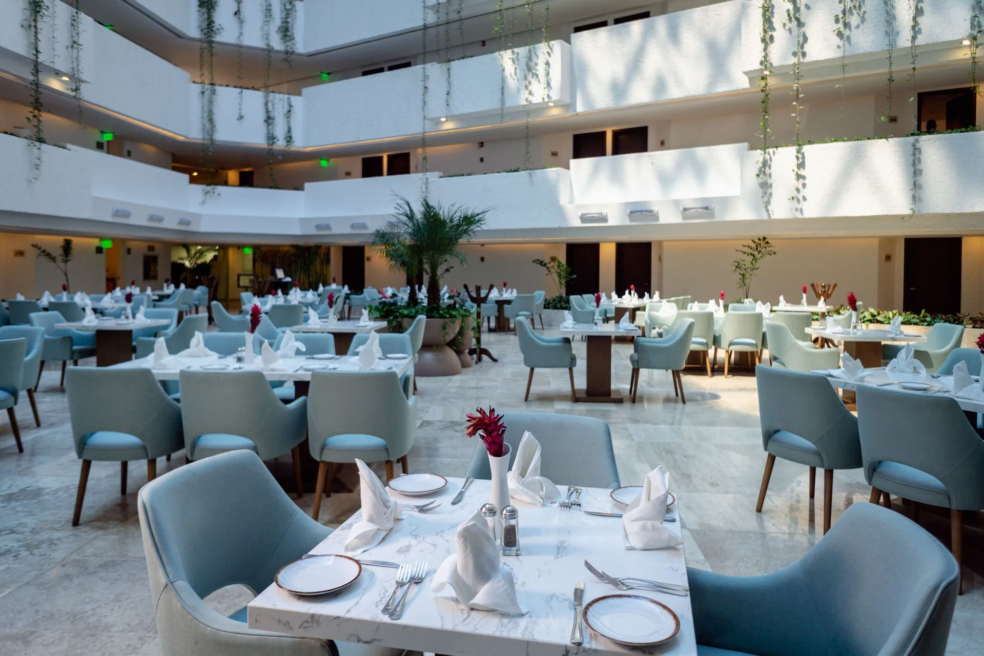 Atrium dining room with set tables and pale blue chairs at Sunset Royal Beach Resort.