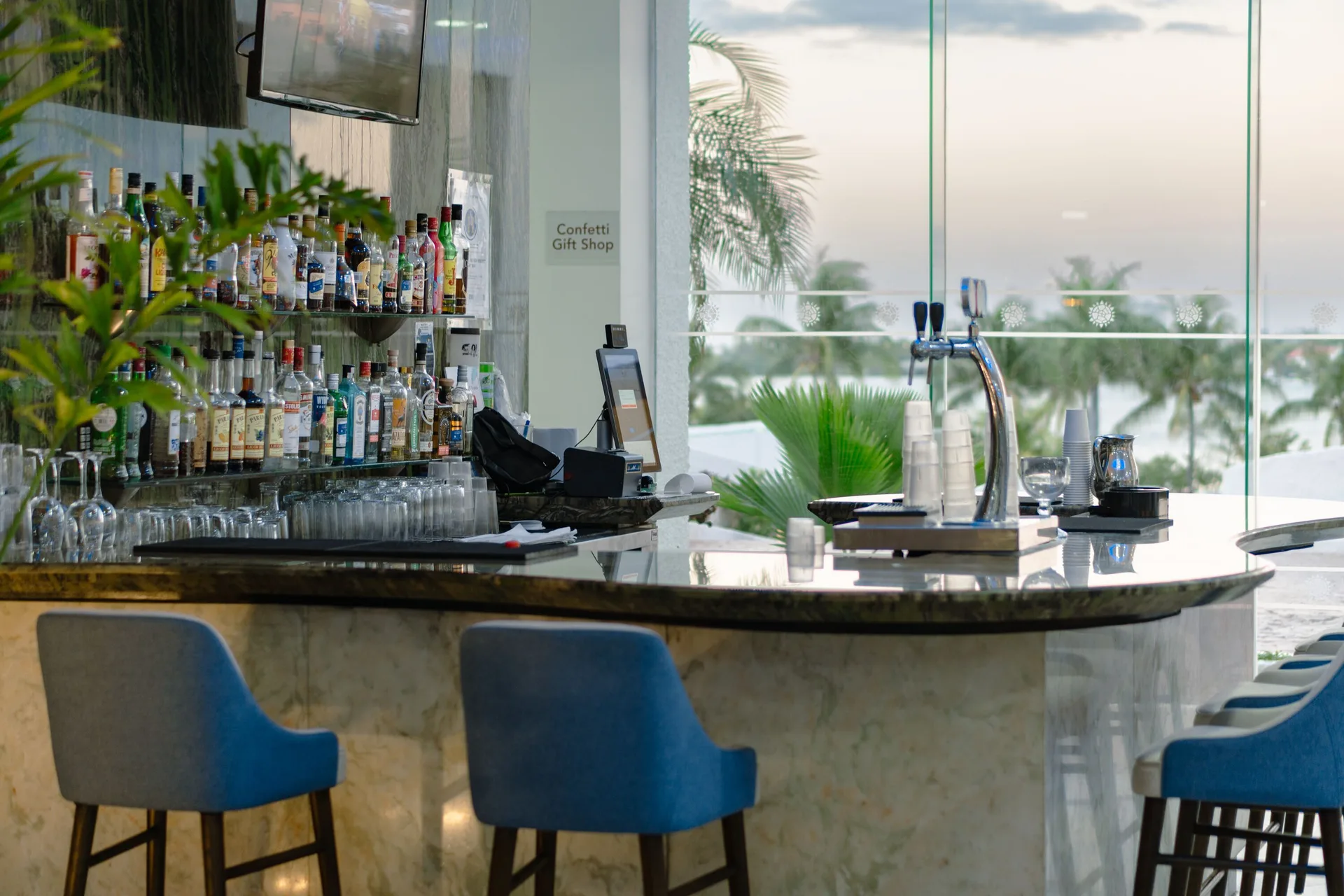 Curved bar with blue stools and ocean-facing windows at Sunset Royal Beach Resort.