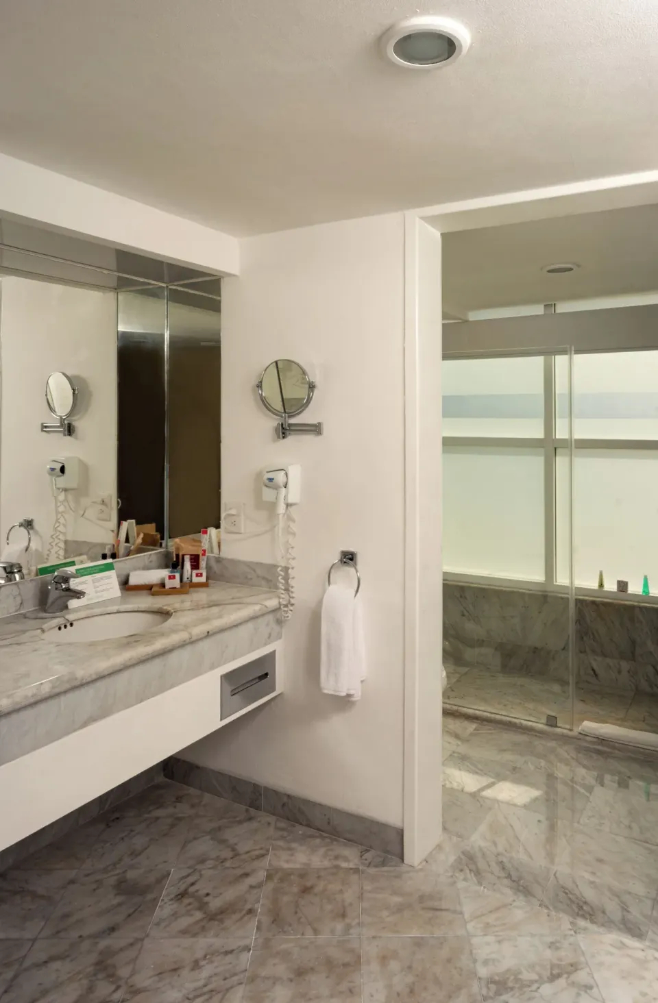 Family Room bathroom vanity with mirror, hair dryer, and shower beyond at Sunset Royal Beach Resort.