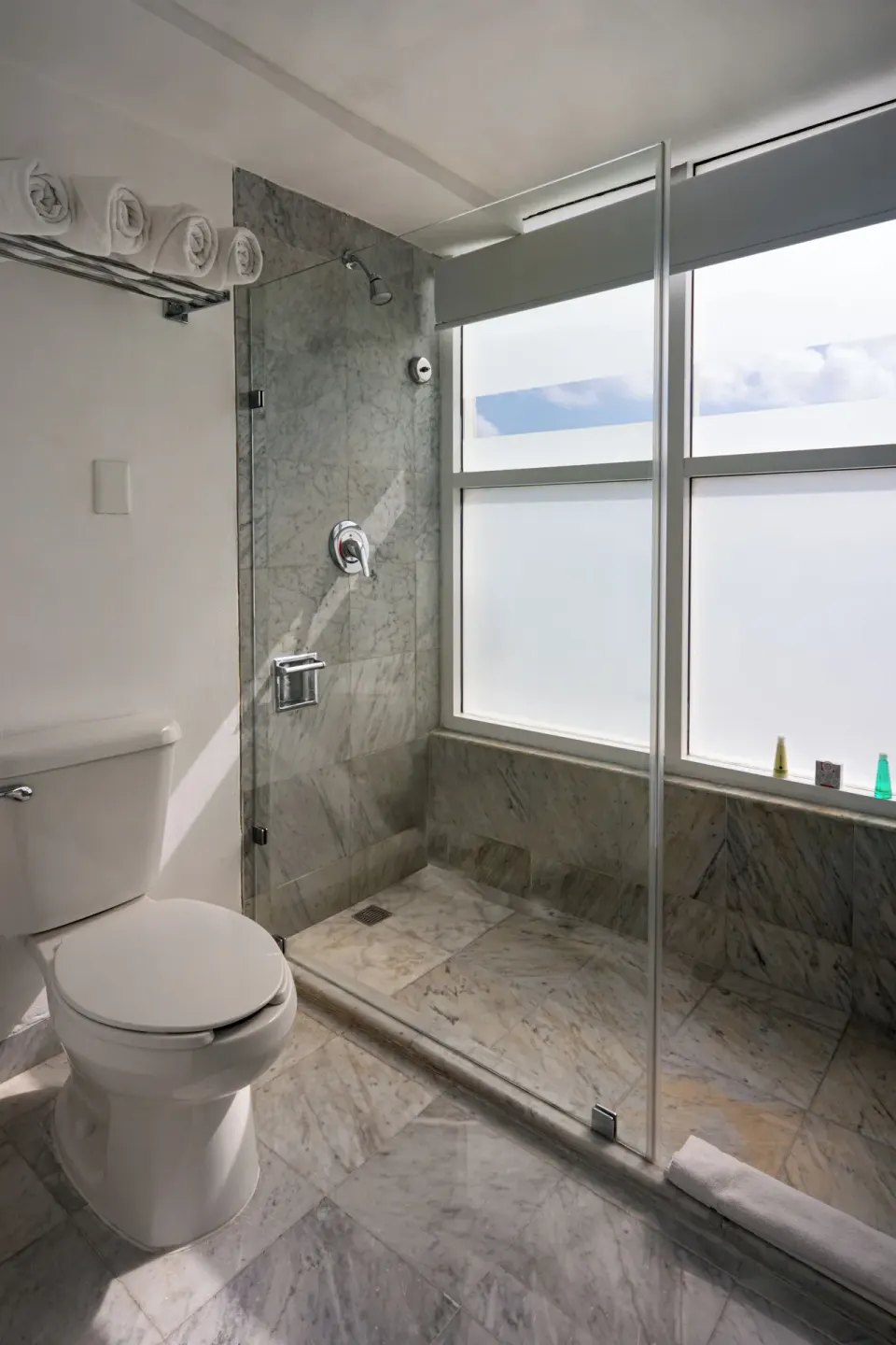 Family Room bathroom shower with glass doors, marble tile, and window at Sunset Royal Beach Resort.