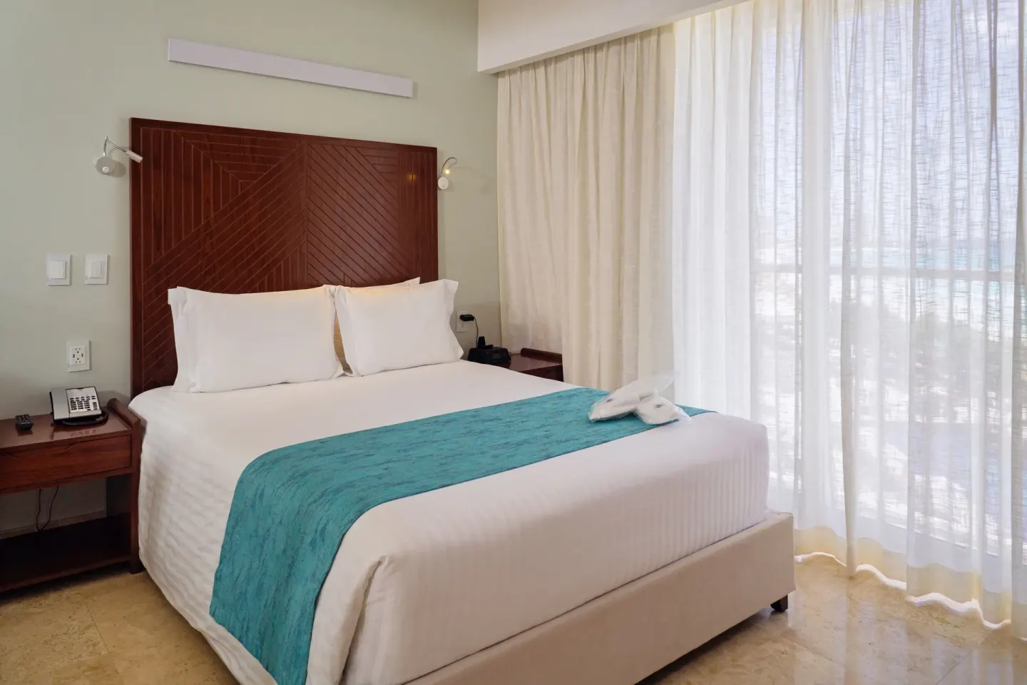 Standard Room bed with turquoise runner and sheer curtains at Sunset Royal Beach Resort.