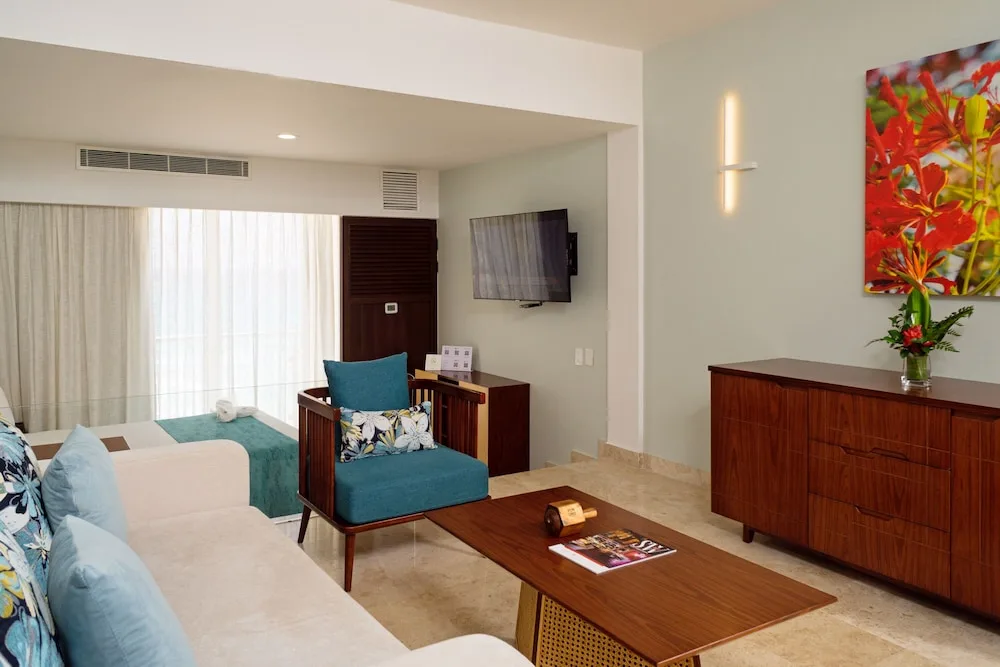 Studio living area with sofa, armchair, TV, and dresser at Sunset Royal Beach Resort.