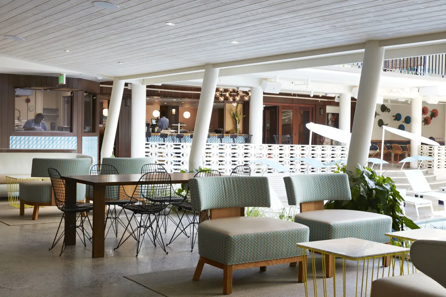 Covered poolside seating area with tables and cushioned chairs at Surfjack Hotel & Swim Club.
