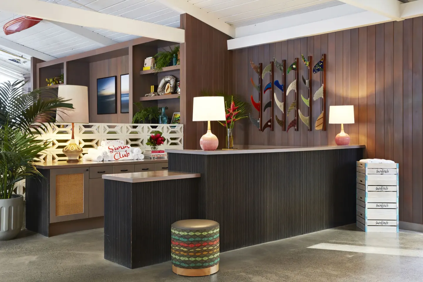 Reception desk with lamps, plants, and surf fin wall art at Surfjack Hotel & Swim Club.