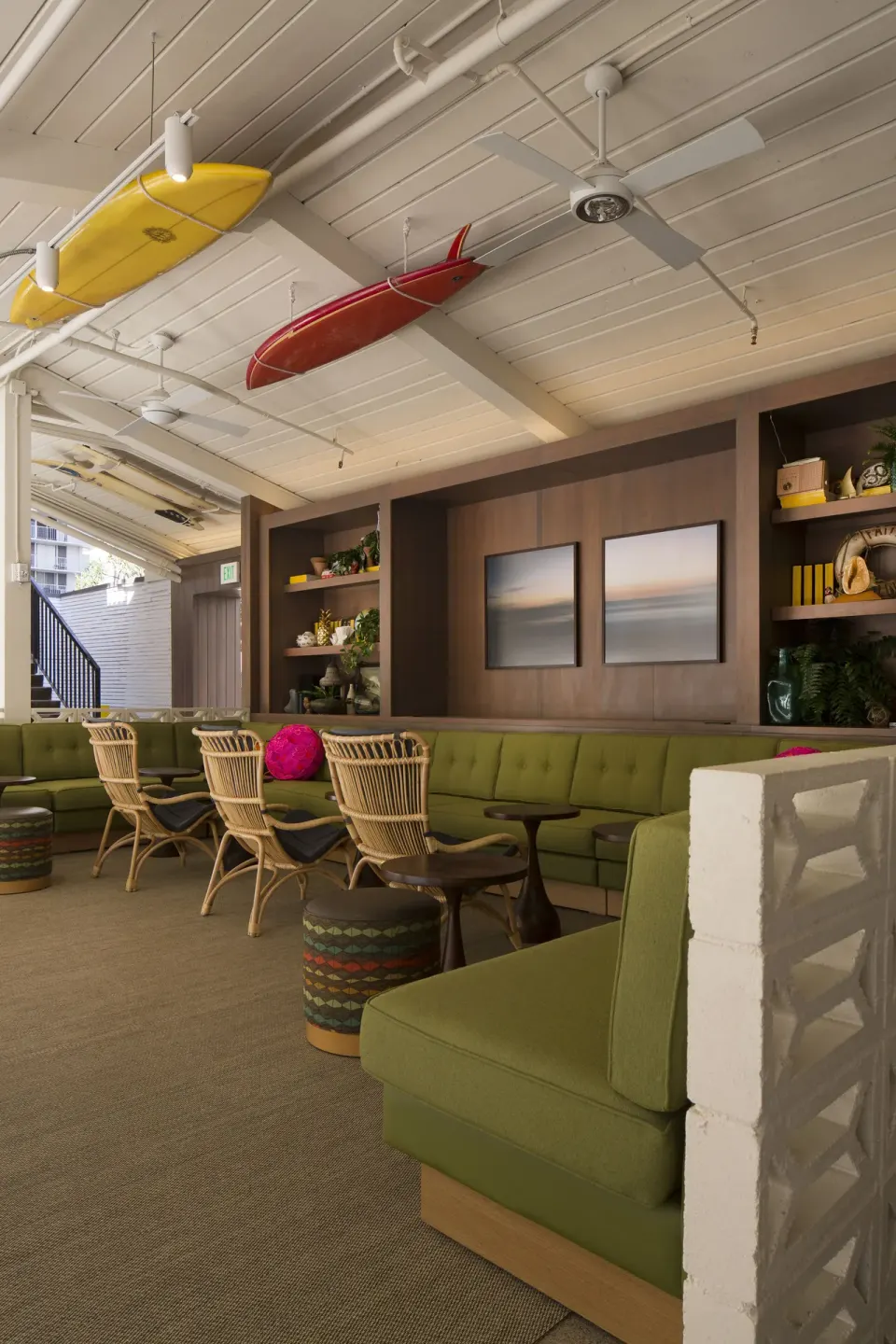 Lounge with green banquettes, rattan chairs, and ceiling surfboards at Surfjack Hotel & Swim Club.