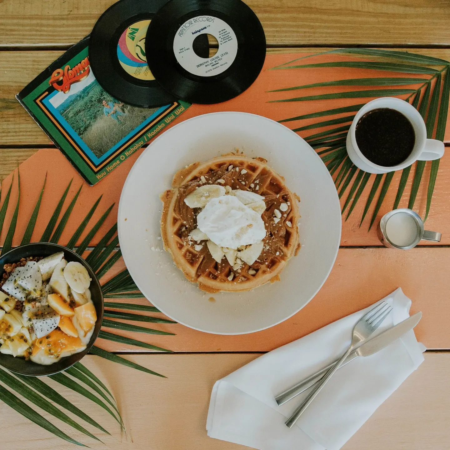 A waffle with fruit, coffee, and records on a tabletop at Surfjack Hotel & Swim Club.