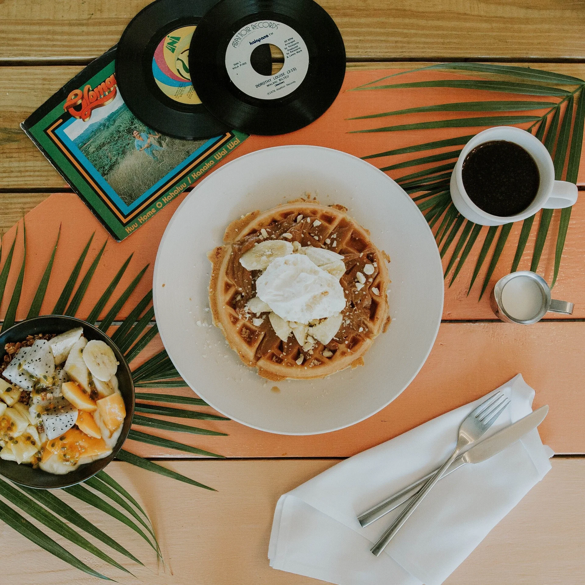 A waffle with fruit, coffee, and records on a tabletop at Surfjack Hotel & Swim Club.