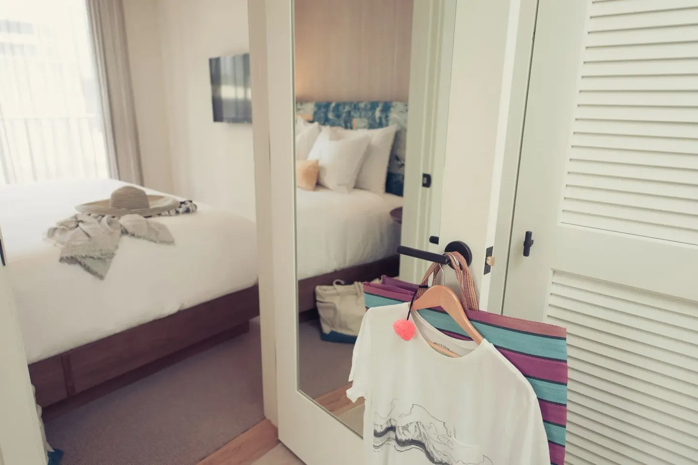 One Bedroom Suite closet mirror and hanging clothes by the bed at Surfjack Hotel & Swim Club.