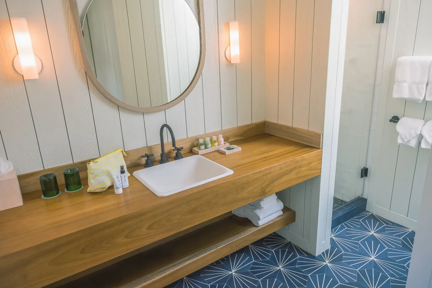 Bathroom vanity with wood counter and glass shower at Surfjack Hotel & Swim Club.