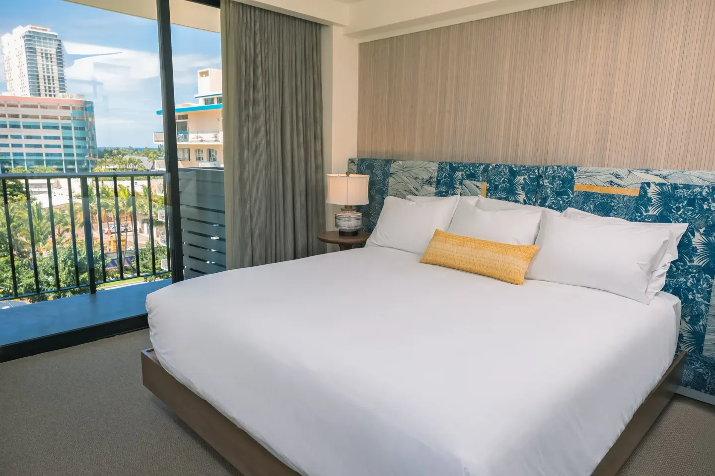 Bedroom with a king bed, patterned headboard, and balcony view at Surfjack Hotel & Swim Club.