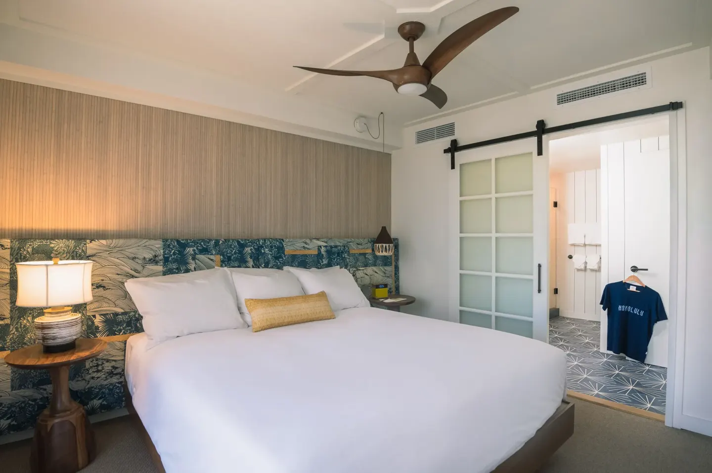 King bedroom with patterned headboard and bathroom doorway at Surfjack Hotel & Swim Club.