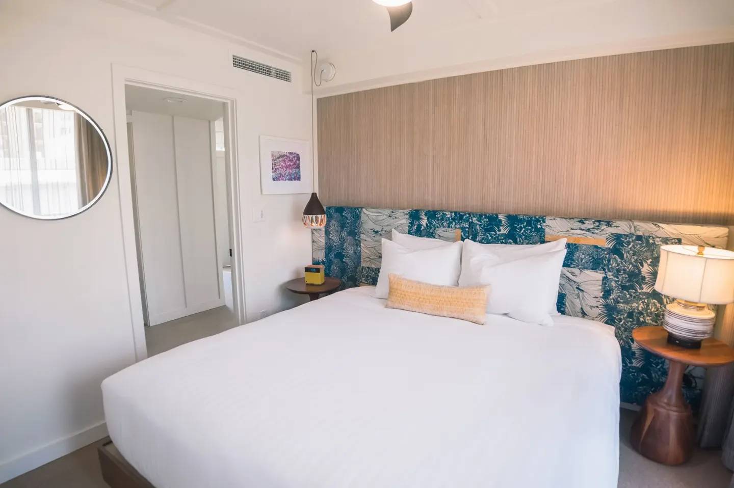 King bedroom with round wall mirror and warm bedside lighting at Surfjack Hotel & Swim Club.