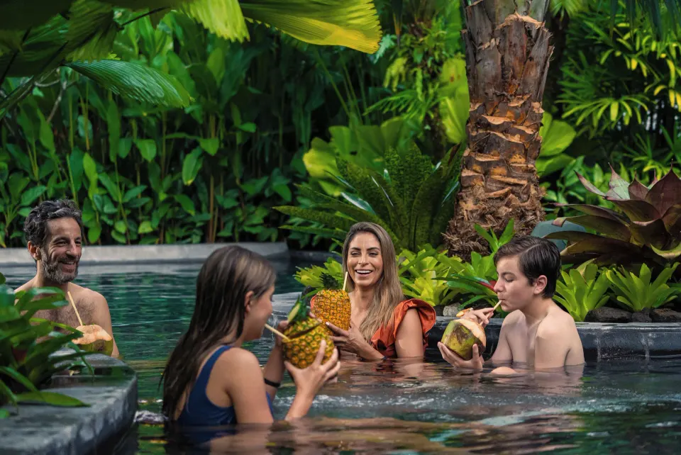 Family relaxing in a jungle pool sipping from coconuts at Tabacón Thermal Resort & Spa