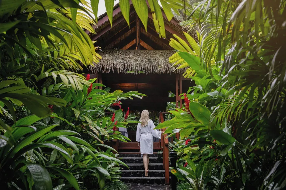Guest in a robe walking up steps through dense tropical plants to a spa bungalow at Tabacón Thermal Resort & Spa
