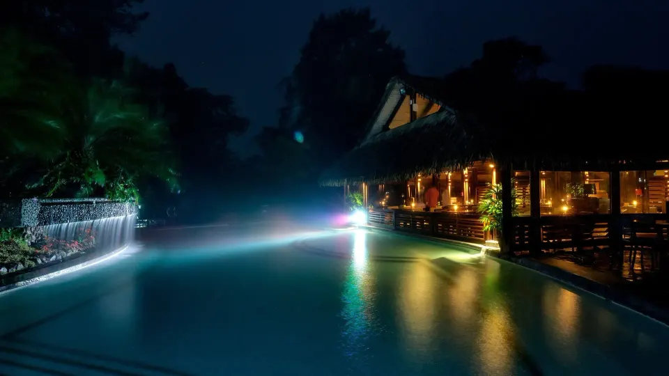 Night view of illuminated pool with waterfall and lit restaurant terrace at Tabacón Thermal Resort & Spa