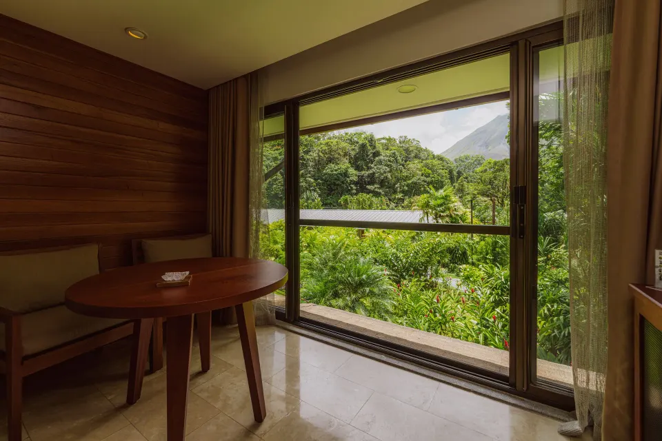 Round table by a large window with dense jungle views in a guest room at Tabacón Thermal Resort & Spa.