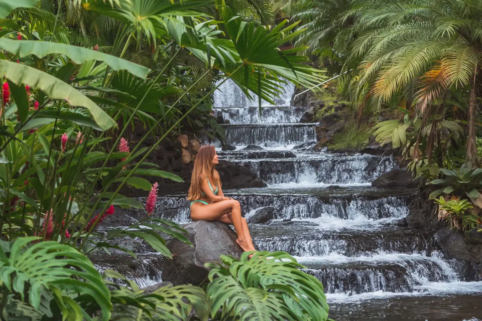 Woman sitting by a tiered waterfall surrounded by tropical plants at Tabacón Thermal Resort & Spa