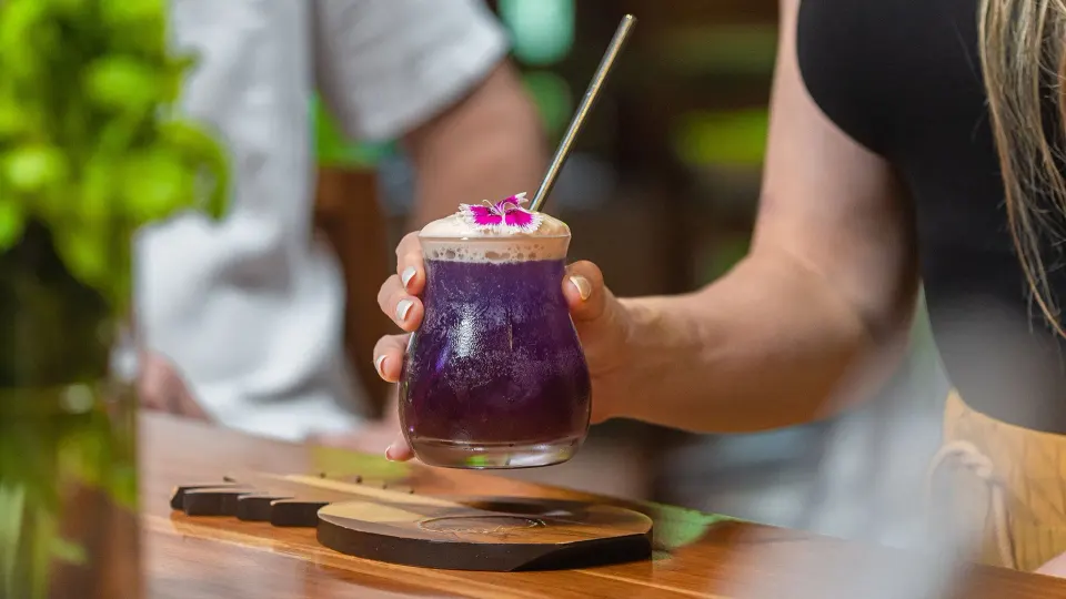 Purple floral cocktail held over a wooden bar at Tabacón Thermal Resort & Spa