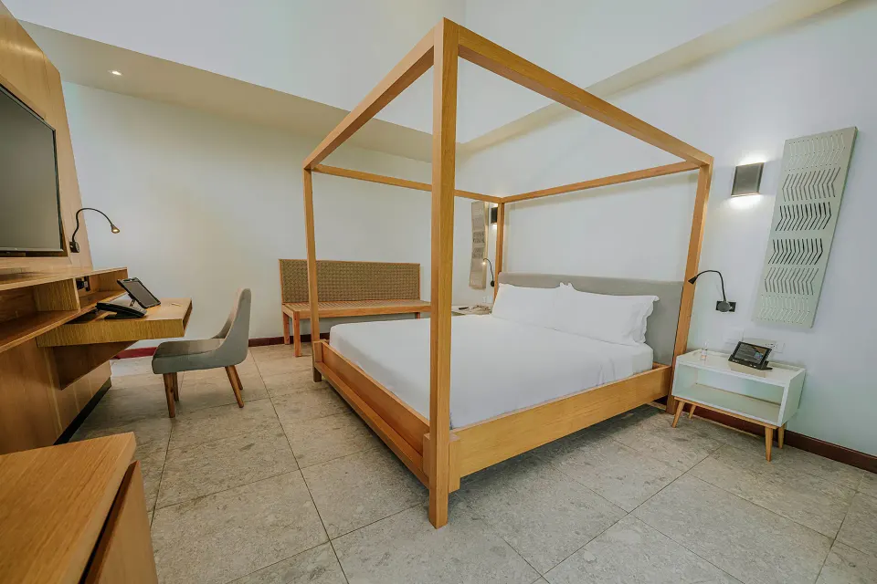 Angled view of four-poster king bed with bedside tables and desk in a Tabacón Suite King Bed Room at Tabacón Thermal Resort &