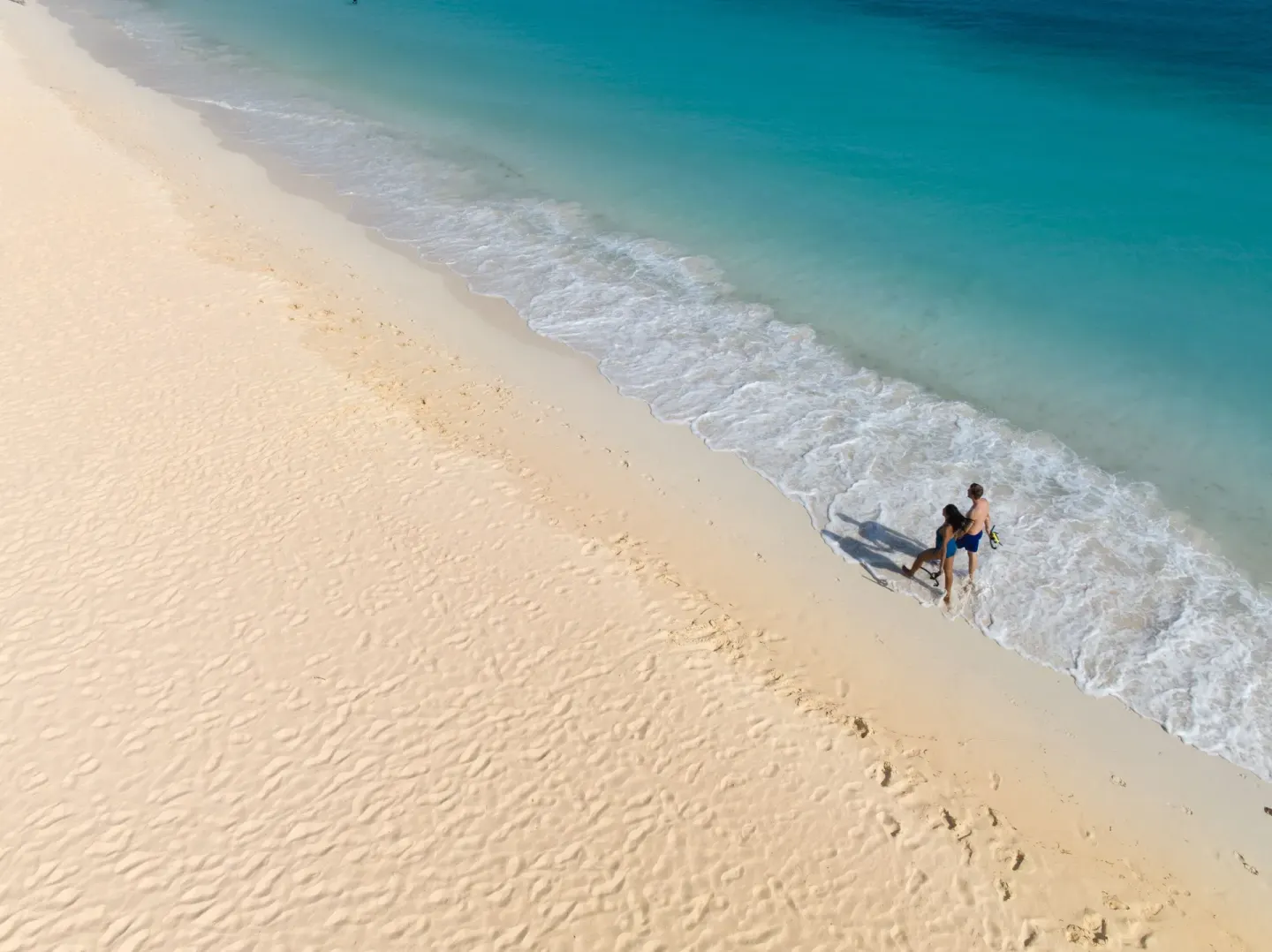 Aerial view of two people walking along the surf at Tamarijn Aruba.