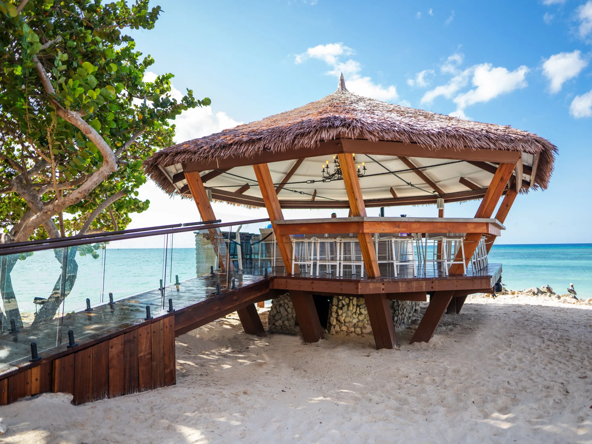 Thatched beach bar with glass-railed walkway beside the sea at Tamarijn Aruba.