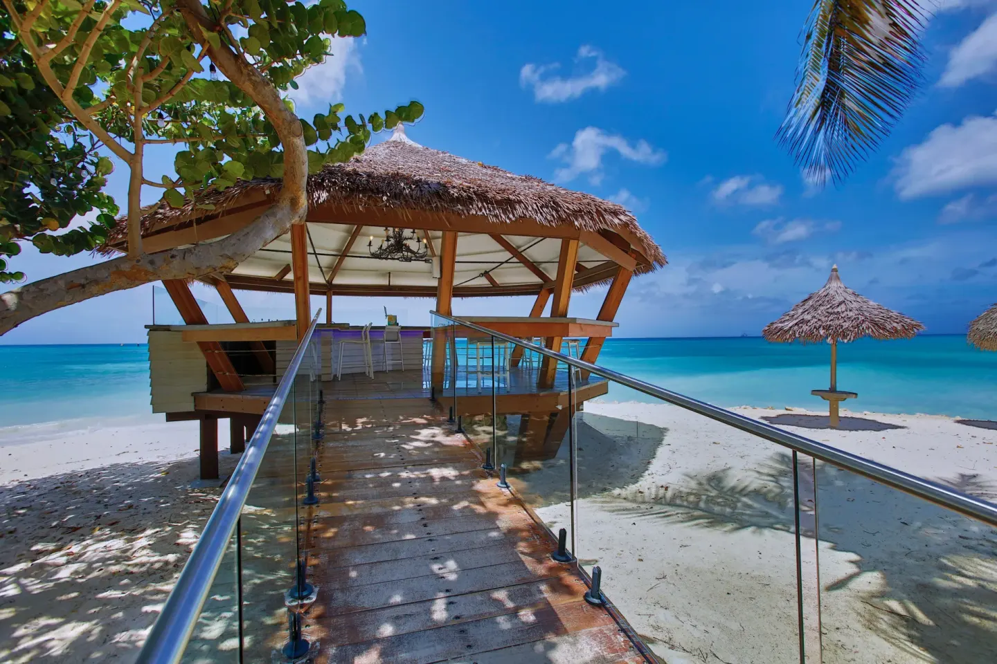 Thatched beach bar over white sand and turquoise water at Tamarijn Aruba.