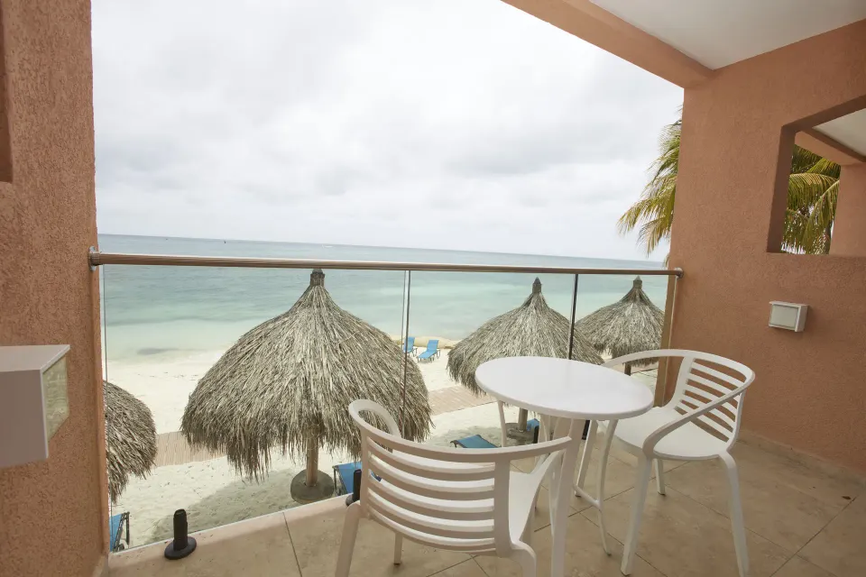 Oceanfront balcony with table, chairs, beach palapas, and sea view at Tamarijn Aruba.