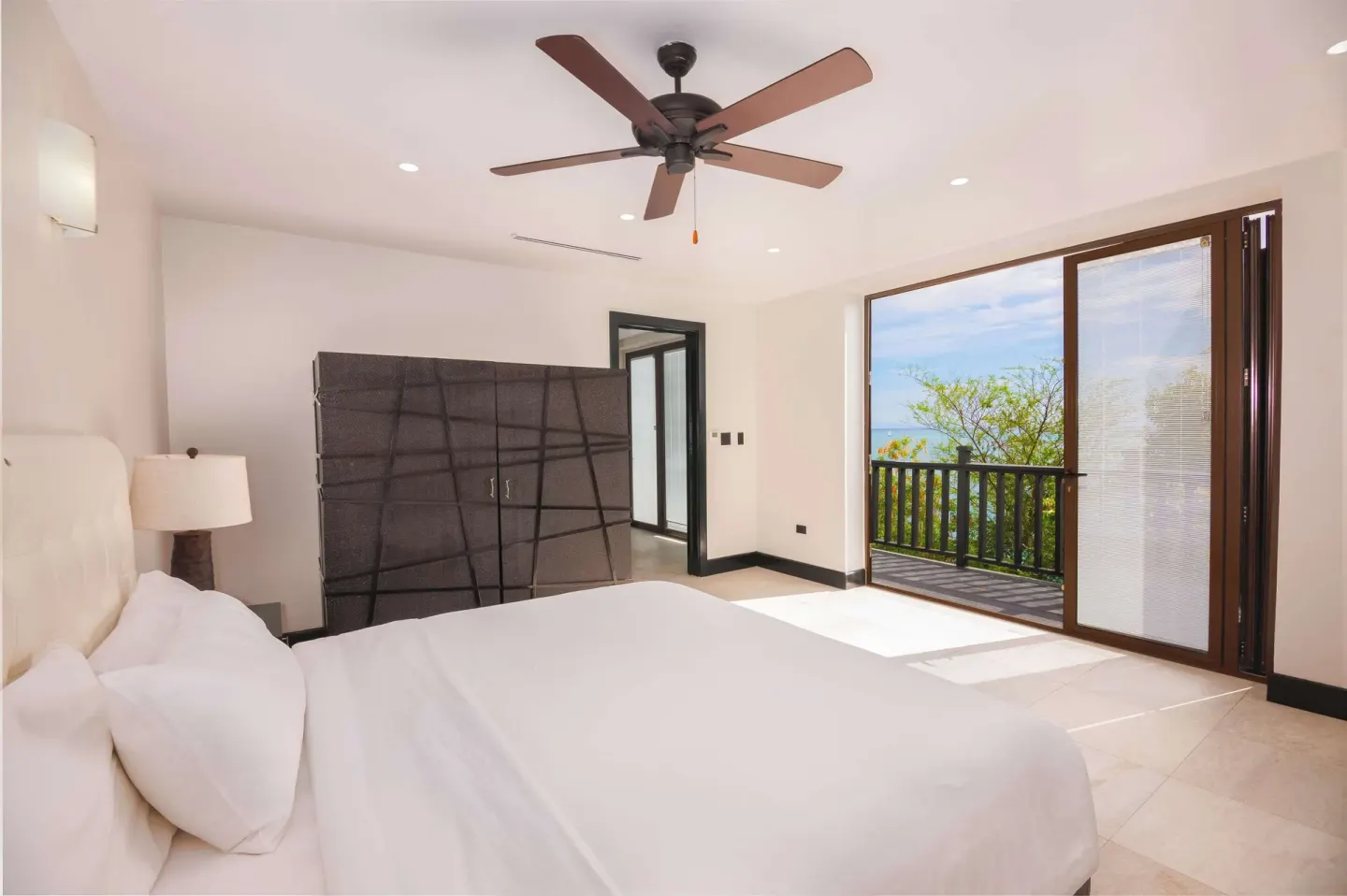 King bed guest room with balcony doors and garden-framed sea view at Tamarind Hills Resort & Villas.