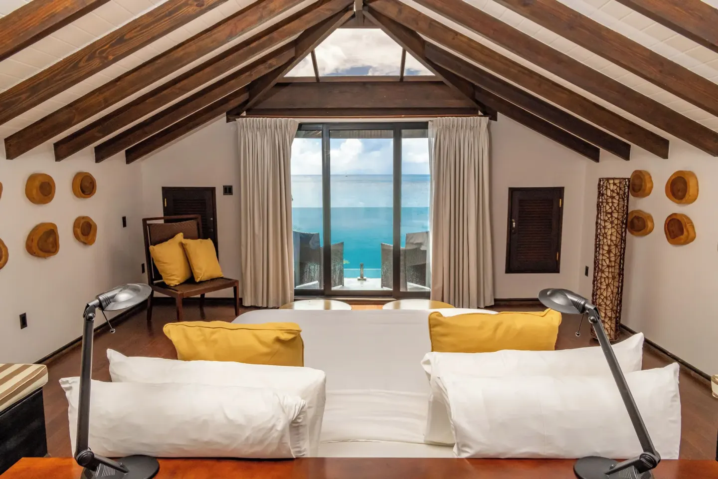 Loft-style guest room with bed, desk lamps and ocean balcony at Tamarind Hills Resort & Villas.