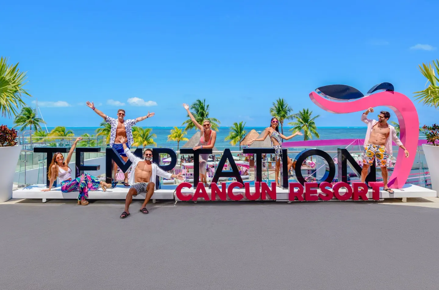 Guests posing with the resort sign and ocean view at Temptation Cancún.