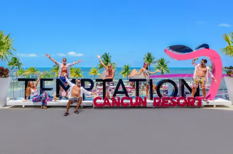 Guests posing with the resort sign and ocean view at Temptation Cancún.