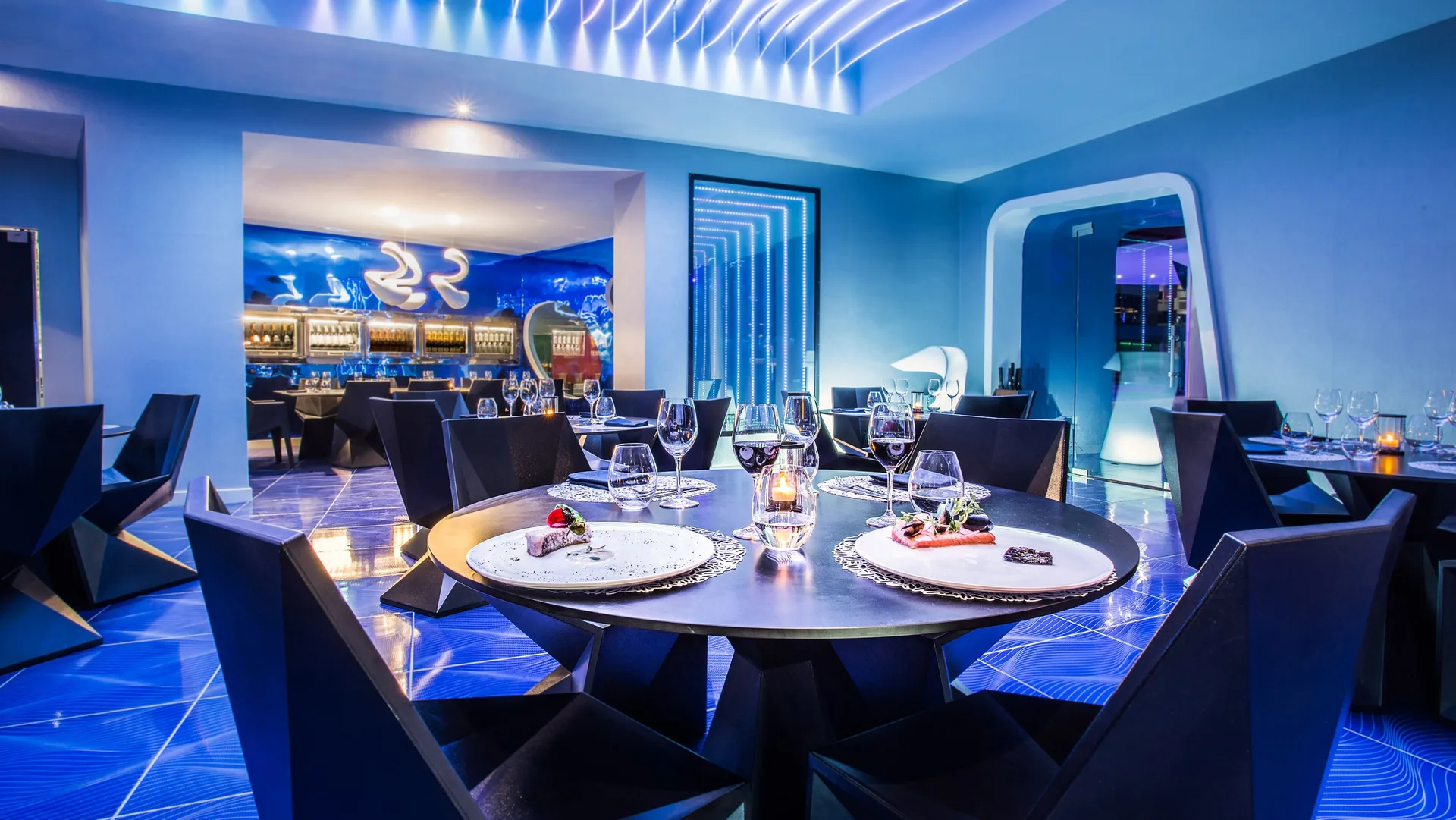Blue-lit dining room with set tables and wine glasses at Temptation Cancún.