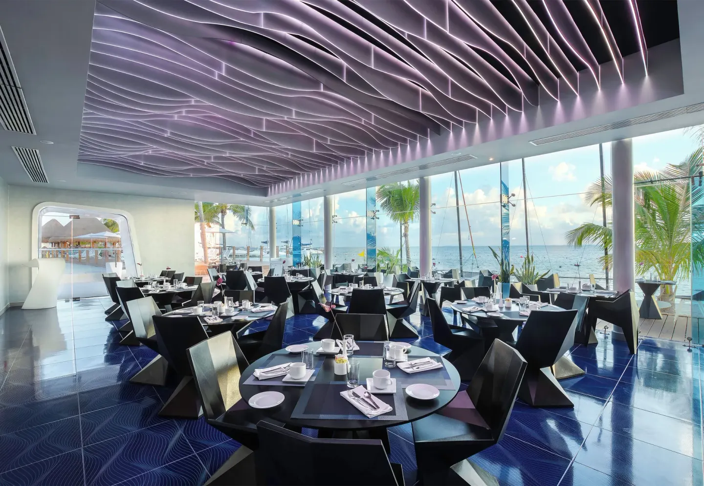 A bright ocean-view dining room with black tables at Temptation Cancún.