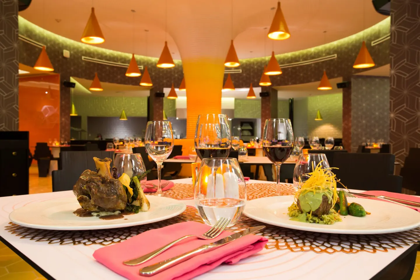 Plated entrees and wine glasses on a restaurant table at Temptation Cancún.