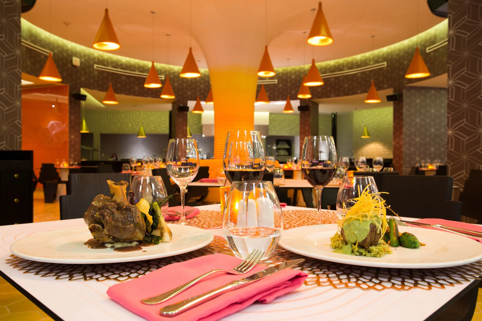 Plated entrees and wine glasses on a restaurant table at Temptation Cancún.