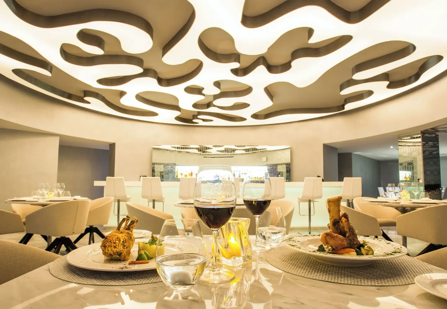 Plated entrees and wine glasses sit in a white dining room at Temptation Cancún.